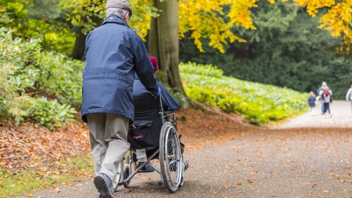 A man pushing a visitor in a wheelchair in the gardens at Fountains Abbey and Studley Royal Water Garden, North Yorkshire